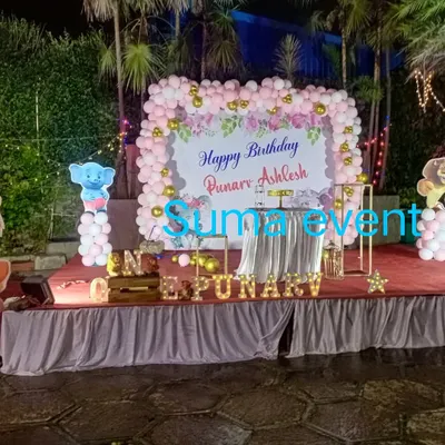 An elegant outdoor stage decoration for Punarv and Ashlesh's birthday. This setup features a large floral backdrop framed by a pink and white balloon arch, set on a professionally draped stage.