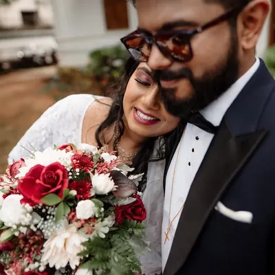 A tender moment between a bride and groom after their ceremony, with the bride holding a beautiful bouquet of red and white roses.