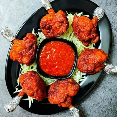 My Chicken Lollypops are crispy on the outside and juicy on the inside. They are served on a bed of shredded cabbage with a side of spicy red dipping sauce.