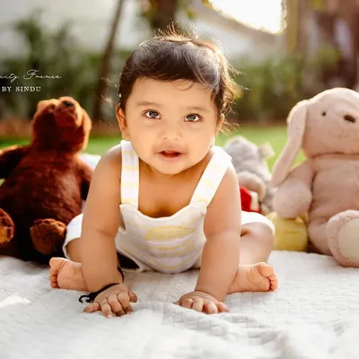 Sunshine and giggles. This outdoor sitter session captures a baby's curiosity as she explores the world around her, surrounded by her favorite stuffed animals.