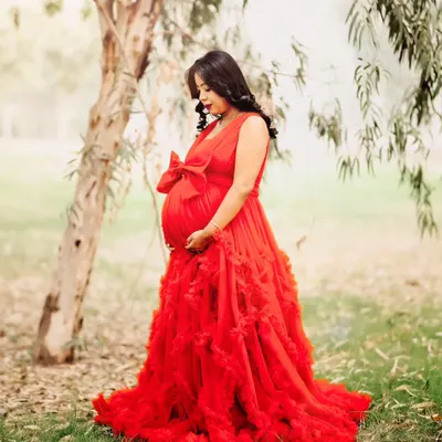 A beautiful outdoor maternity portrait taken in a lush, green park. The mom-to-be looks serene in a flowing red gown, creating a stunning contrast with the natural surroundings.