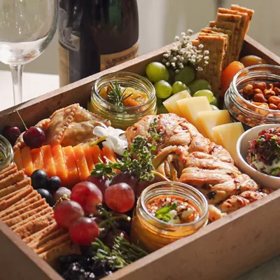 A stunning overhead view of our Cheese & Dip Grazing Box. This ready-to-serve box is filled with an assortment of cheeses, fresh grapes, cherries, savory crackers, spiced nuts, and our signature house dips.