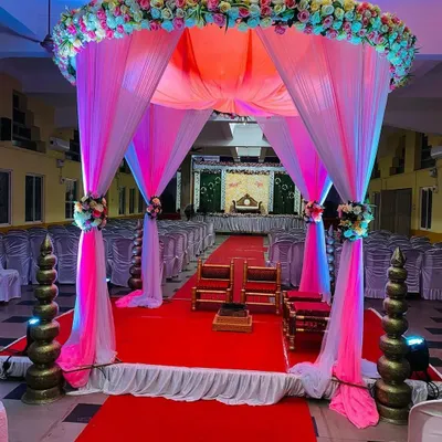 A breathtaking view down the aisle towards the wedding mandap. The entrance is framed by a canopy of pink and white drapes and flowers, creating a grand and romantic pathway for the ceremony.