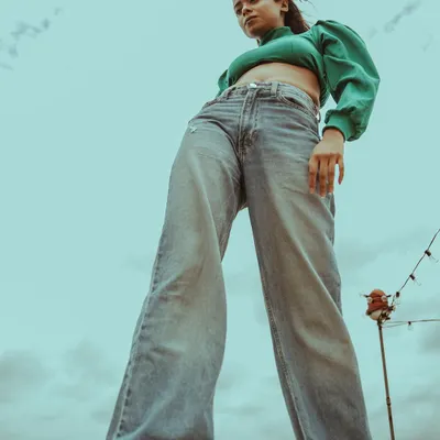 A low-angle shot that creates a powerful and confident look. The combination of a green puff-sleeve top and wide-leg jeans against the open sky gives this portrait a bold, modern edge.