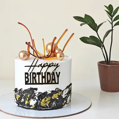 A modern birthday cake with a black, white, and gold abstract design at the base. The cake is topped with a pulled isomalt sugar sail and gold spheres for an artistic touch.