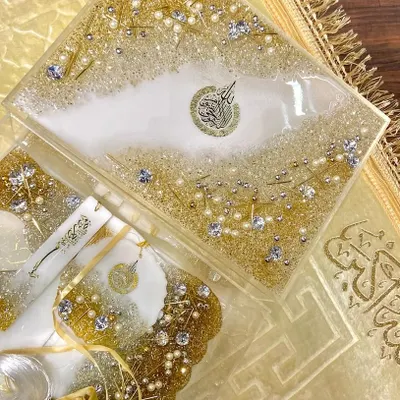 An elegant gift set in white and gold, perfect for Eid or any special occasion. This set includes a resin Quran box, a matching bookmark, and other accessories, all embellished with crystals and pearls for a luxurious finish.