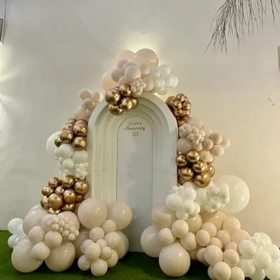 Elegance for a milestone celebration. This custom anniversary backdrop features a sophisticated organic balloon garland in nude, white, and chrome gold tones, creating a perfect photo opportunity for the happy couple.