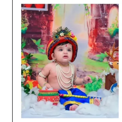 A serene portrait of a baby boy dressed as Little Krishna, looking up with a gentle expression. The detailed costume, including pearl necklaces and a peacock feather crown, is perfect for a Janmashtami theme.