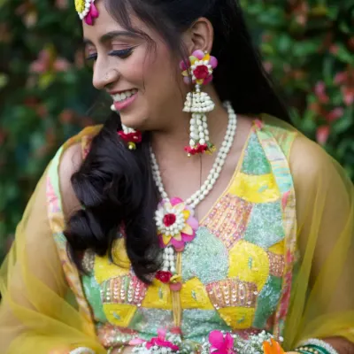 A close-up of this bride's happy smile and her colorful floral jewellery. The jhumkas and necklace perfectly match the vibrant kalire, creating a joyful and coordinated look.