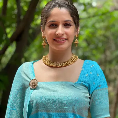 The beautiful Thejaswini Sharma looks so graceful in this classic gold-tone necklace set. This style is perfect for adding a touch of timeless elegance to a saree or any ethnic outfit. The set comes with a traditional beaded choker and matching jhumka earrings.
