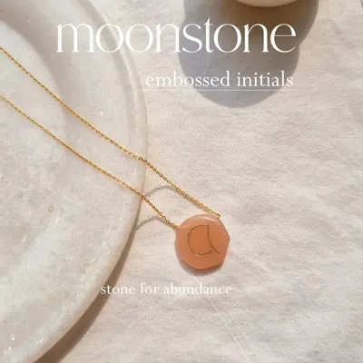 My signature initial pendant, featuring a custom-embossed letter on a hand-shaped Peach Moonstone. This piece is designed to be a deeply personal and grounding accessory for daily wear.