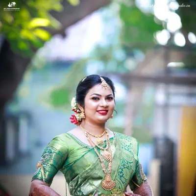 A radiant bridal portrait captured outdoors. The natural light beautifully highlights the rich green of her silk saree and the intricate gold jewelry.