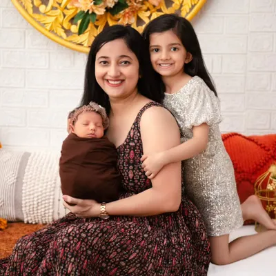 A mother sits with her older daughter, who lovingly embraces her and the new baby. This portrait highlights the joy of a growing family, capturing the special bond between a mother, her first child, and the newest arrival.
