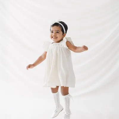 Pure, uncontainable joy. This little girl, celebrating her second birthday, is captured mid-jump, perfectly showing the energy and happiness of being a toddler. The all-white, minimalist setup makes her joyful expression pop.