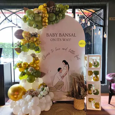 A beautiful, personalized baby shower backdrop for Baby Bansal. The custom illustration of the parents-to-be adds a deeply personal touch, complemented by an elegant olive green and gold balloon arch.