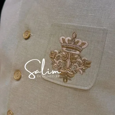 A close-up of the hand-embroidered crown crest on a beige Jodhpuri jacket. This kind of custom detail adds a regal and personal touch to your outfit.