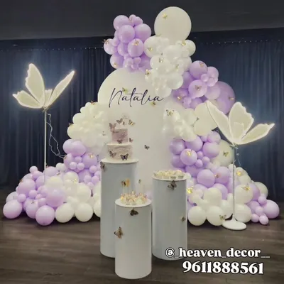 An elegant and ethereal butterfly theme in lavender and white, perfect for any age. The setup features an organic balloon cloud, large illuminated butterfly props, and minimalist white plinths for a sophisticated look.