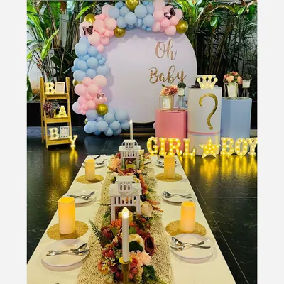 A beautiful baby shower setup combining a dining table arrangement with a photo backdrop. The 'Oh Baby' installation features a pastel balloon arch and marquee lights for the gender reveal.