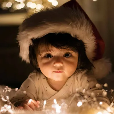 A close-up portrait of a newborn celebrating their first Christmas. We used soft fairy lights and a festive Santa hat to create this warm, magical moment, highlighting the baby's innocent expression.
