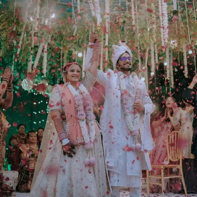 A moment of pure triumph and joy. As flower petals rain down, the newly married couple raises their hands in celebration, surrounded by the love of their family and friends.