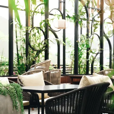A close-up on the details. The interplay of textures, from the woven chairs to the lush greenery, creates a rich visual narrative about the cafe's design aesthetic.