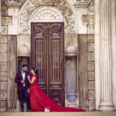 Create a timeless pre-wedding portrait with this stunning maroon-red floral gown. Paired with a classic men's blazer, it makes for a powerful and romantic couple's look against a grand architectural backdrop.