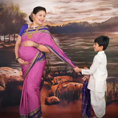 Inspired by the classic paintings of Raja Ravi Varma, this studio portrait features a mother-to-be and her son in traditional attire. The painted landscape backdrop and soft lighting create a timeless, artistic feel.