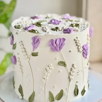 A little garden in bloom, but make it cake. This design features hand-piped lavender and white wildflowers, creating a delicate and artistic floral pattern around the entire cake.