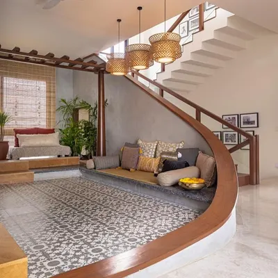 This living area features a modern take on the traditional 'thinnai' or raised verandah seating. The curved, built-in bench is paired with patterned floor tiles and woven pendant lights for a look that is both contemporary and classic.