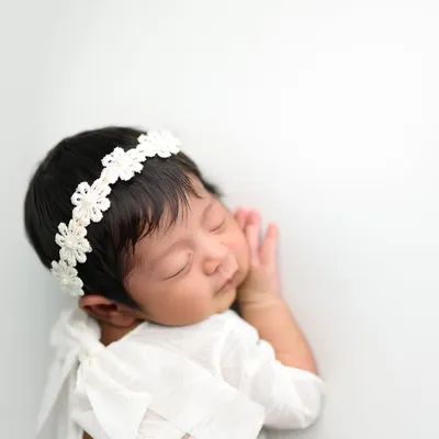 A portrait of pure serenity. This little one is posed to showcase their delicate features and peaceful sleep, using a simple white-on-white setup for a timeless and classic newborn photograph.