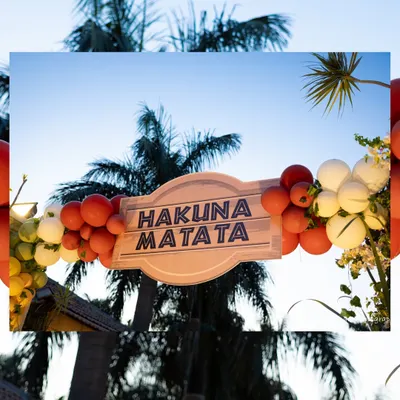 A "Hakuna Matata" sign framed by a sunset-colored balloon arch against a backdrop of palm trees perfectly captured the carefree spirit of The Lion King.