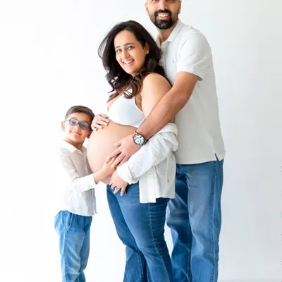 A heartwarming family maternity photo where an older sibling joins his parents to embrace the baby bump. This shot captures the excitement of the entire family in a clean, modern studio style.