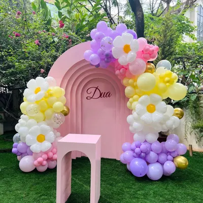 A pretty garden setup for Dua's first birthday, featuring a pink arched backdrop with her name. The daisy-shaped balloon clusters add a whimsical and charming touch to the outdoor decor.