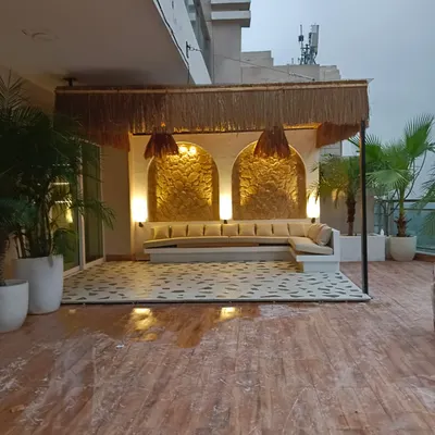 This Moroccan-inspired terrace features a beautiful cabana with intricate golden back panels and a comfortable L-shaped sofa. The design creates a luxurious, resort-like feel.