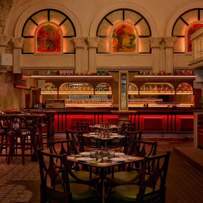 The main dining area of Los Cavos, where the red-lit bar creates a dramatic focal point. The design uses arched windows and warm ambient lighting to craft an intimate yet grand atmosphere, reminiscent of colonial Cuban architecture.