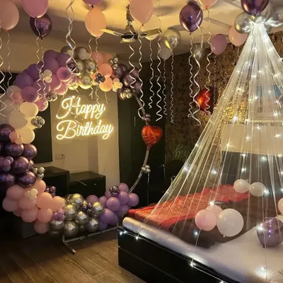 A romantic birthday surprise in the bedroom. This setup features a bed canopy with fairy lights, a half-arch of balloons in purple and pink, and a "Happy Birthday" neon sign.