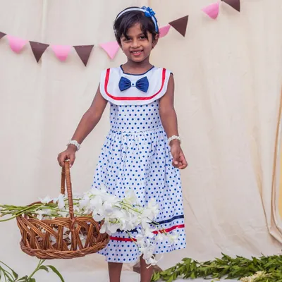 A classic look for a sunny day. This white and blue polka dot dress with a sailor collar is perfect for a picnic or a stroll, and she looks adorable holding a basket of flowers.
