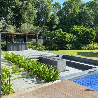 A modern farmhouse landscape featuring a sunken seating area with an integrated fire pit adjacent to the pool. This design creates distinct zones for relaxation and entertainment, surrounded by lush plantings and an outdoor bar for a complete resort-like experience at home.