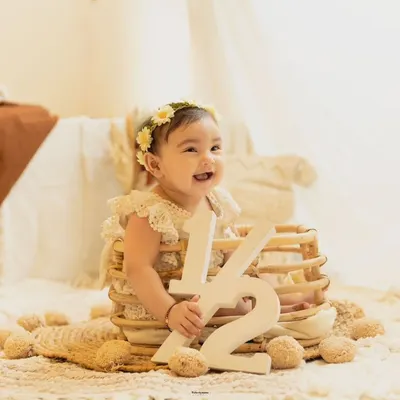 Celebrating six months. This happy baby girl marks her half-birthday with a '1/2' sign in a beautiful, bohemian-style studio setup.