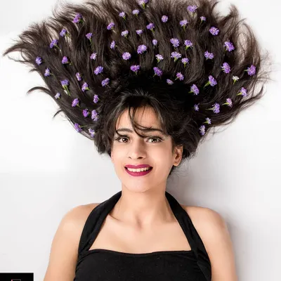 A creative overhead portrait with the model's hair spread out and adorned with small purple flowers. Her expressive face and the unique styling make this a standout artistic shot.