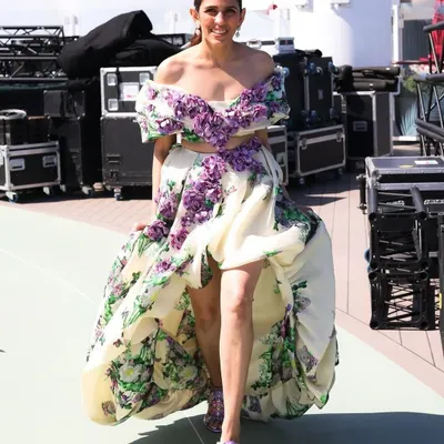 This Yara Shoemaker floral gown is pure romance. The off-shoulder design, 3D floral details, and high-low skirt make it a perfect statement piece for a summer gala or a destination event.
