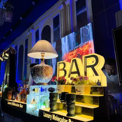 A close-up of our bar decor, featuring large illuminated 'BAR' letters, quirky tiki mugs, and an elegant vintage-style lamp.