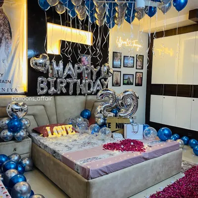 An elaborate and romantic 29th birthday room decoration. The setup includes balloons on the ceiling, 'Happy Birthday' and number foils, a 'LOVE' marquee light, and a rose petal pathway.
