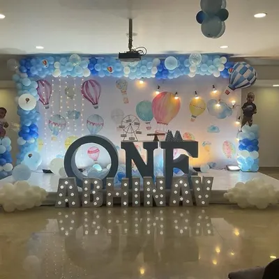 A spectacular hot air balloon themed stage for a first birthday. The grand setup includes marquee lights, multiple balloon pillars, and a wide backdrop depicting a sky full of hot air balloons.
