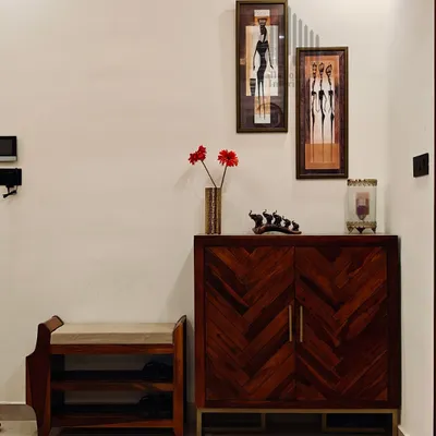 A warm and welcoming foyer featuring a chevron-patterned wooden shoe cabinet and a matching bench, complemented by ethnic art pieces.