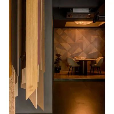 A view into a private discussion nook within the veneer showroom. The wall is clad in a geometric veneer pattern, creating a sophisticated and moody atmosphere for client meetings.