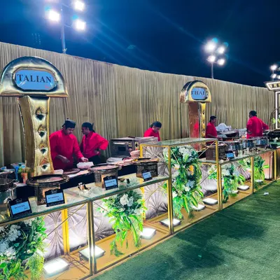 An overview of our elegant Italian food counter at an outdoor evening event. The setup features gold and white decor, beautiful floral arrangements, and dedicated chefs ready to serve fresh pasta and other Italian specialties.