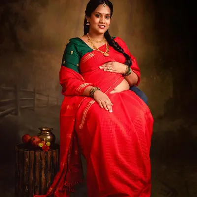 A classic portrait celebrating motherhood in a beautiful red saree. The painted backdrop and traditional props in my studio help create a timeless, regal look.