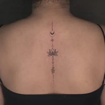 An elegant and beautiful spine tattoo. This fine-line design uses minimalist symbols like the moon, lotus, and unalome to create a piece that flows perfectly with the body's natural curvature.