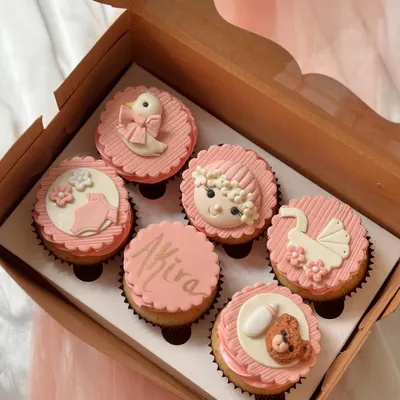 A personalized baby shower gift box in a pink theme. This set includes a cupcake with the name 'Akira' and other fondant designs like a baby face, a pram, a duck, and a teddy bear, showing a fully customized order.